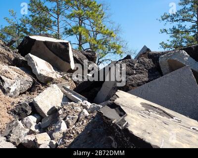 Montagna di asfalto, fondo stradale in cemento e detriti di parcheggio nel sito di demolizione stradale, alberi di pino in background, vista media ampia Foto Stock