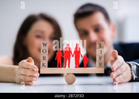 Coppia felice la protezione di equilibrio tra lavoro e vita familiare e carta ritagliata su altalena Foto Stock