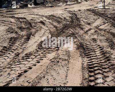 Attrezzature pesanti cingoli di pneumatici in sabbia nel sito di demolizione stradale, enormi larghe piste sovrapposte, mucchio di macerie stradali sullo sfondo, ampia visuale Foto Stock