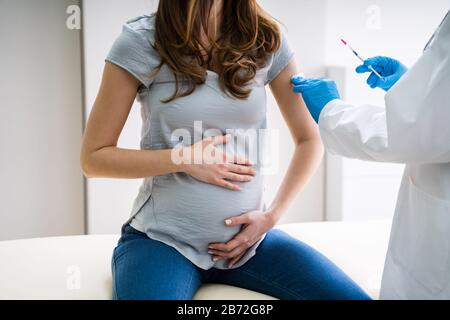 Close-up di medico indossando guanti blu la vaccinazione di giovane donna incinta in clinica Foto Stock
