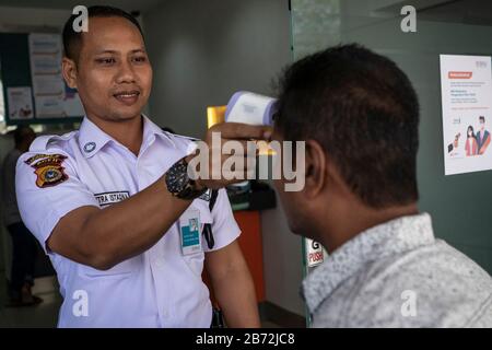 Lhokseumawe, Aceh, Indonesia. 13 Marzo 2020. Gli agenti di sicurezza controllano la temperatura corporea di un uomo prima di entrare in un ufficio di servizio a Lhokseumawe, provincia di Aceh. Il governo indonesiano ha confermato 34 casi di coronavirus COVID-19 con un decesso confermato. L'Organizzazione Mondiale della Sanità (OMS) ha dichiarato la diffusione del coronavirus scoperto più di recente, che causa la malattia COVID-19, una pandemia il 11 marzo 2020. Credit: Zikri Maulana/Zuma Wire/Alamy Live News Foto Stock