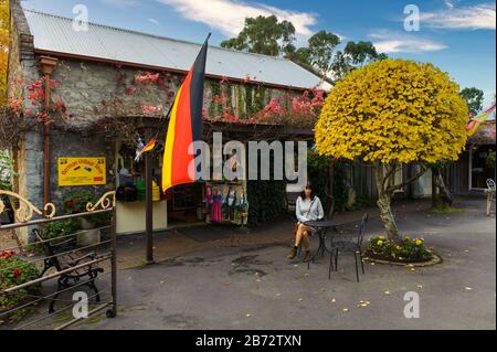 Single femminile turistica si trova di fronte a un vecchio negozio di pietra che porta una bandiera tedesca in attesa del suo caffè circondato dalla flora autunnale Foto Stock