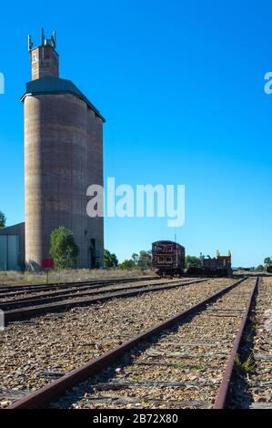 I vecchi binari ferroviari storici che portano a nord lontano da Quorn in Australia del Sud, oltrepassano un vecchio silo, un capannone merci e un paio di carrozze ferroviarie d'epoca. Foto Stock