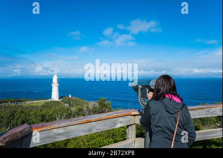 Vista del Faro di Cape Otway a Victoria, Australia come turista femminile gode della spettacolare scena dell'Oceano Meridionale dietro le rotaie di guardia Foto Stock