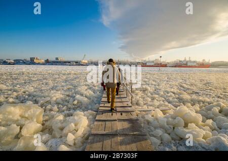 Un uomo cammina sulle tavole attraverso una traversata di ghiaccio. Attraversando un fiume ghiacciato. Russia, Arkhangelsk Foto Stock