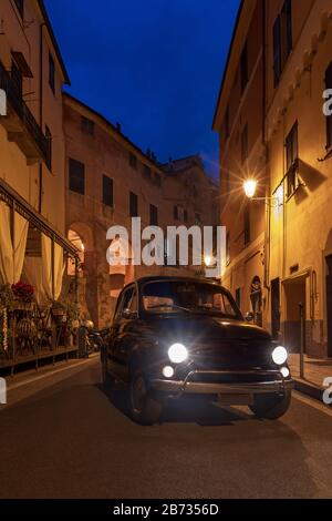 Auto classica in crociera su una strada del centro storico di Imperia di notte Foto Stock