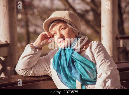 Un'elegante donna anziana dai capelli grigi siede su una panchina del Parco. Foto Stock