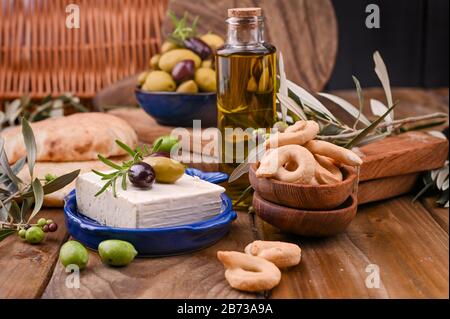 Formaggio greco con olive e CRACKER italiani e ITALIANI o TARALLI . Rami d'oliva freschi, olio d'oliva in bottiglia con spuntini tradizionali italiani. Spazio di copia Foto Stock