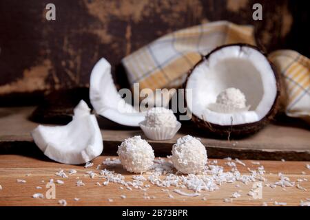 Primo piano di cocco con polpa bianca, scaglie di cocco e tartufi di cocco dolce al cioccolato. Guscio di cocco, fiocchi di cocco, piccoli pezzi di dado schiantato, co Foto Stock