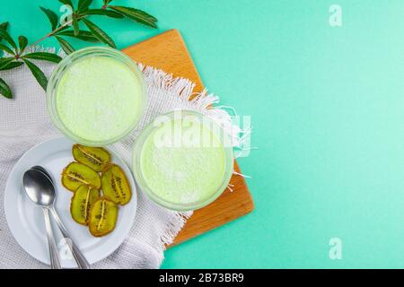 Yogurt di limone alla menta con kiwi in ciotole per insalata su una tavola di legno con rami verdi su uno sfondo rosa Foto Stock