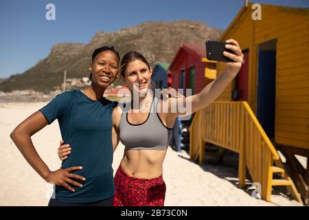 Vista frontale di amici che prendono selfie alla spiaggia Foto Stock