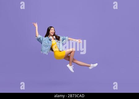 Giovane bella ragazza asiatica sorridente galleggiante a mezz'aria con la mano che punta su e giù isolato su sfondo viola Foto Stock