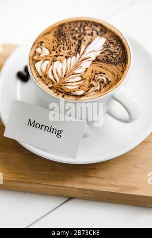 Fern pattern latte art caffè in tazza accanto testo di saluto su vassoio di legno in caffè Foto Stock