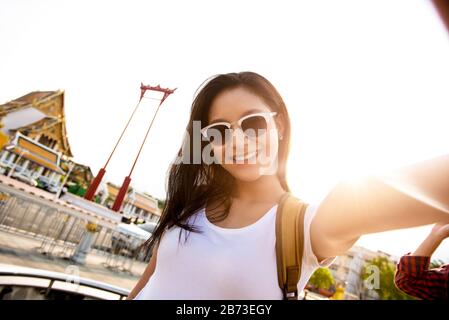Sorridente giovane bella donna asiatica che indossa occhiali da sole prendendo un selfie al Giant Swing mentre si viaggia a Bangkok Thailandia