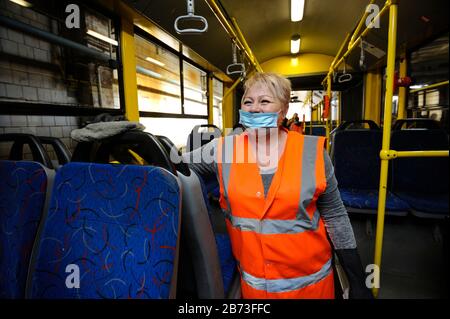 Sorridente operaio in maschera protettiva disinfettante l'interno del filobus da coronavirus, deposito trolley bus. 11 marzo 2020. Kiev, Ucraina Foto Stock