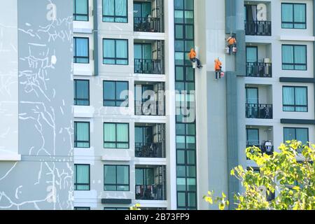 Tre operai con accesso a corda dipingere la facciata di un alto edificio moderno Foto Stock