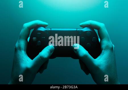 Foto di scorta delle mani che tengono un gamepad nero con una luce blu Foto Stock