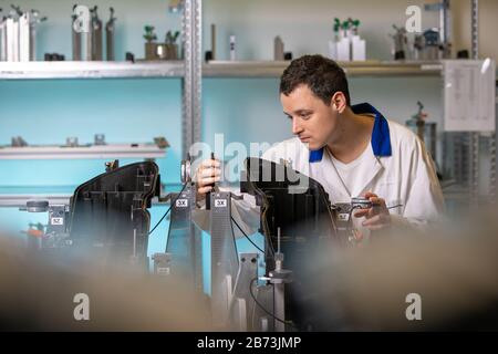 L'ingegnere misura i componenti in plastica per la produzione di luci per l'industria automobilistica in una fabbrica su una macchina digitale 3D Foto Stock