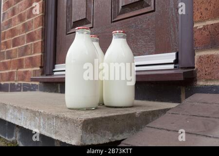 Latte fresco in biberon di vetro riciclabile consegnato alla porta da un tradizionale lattiere Foto Stock