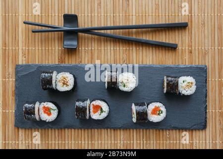 Sushi su una tavola di pietra nera. Sushi fresco con salmone e avocado e anguilla. Cucina tradizionale giapponese. Foto Stock