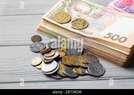 Denaro dell'Ucraina. Pila di banconote ucraine di hryvnia con diverse monete piccole su tavolo di legno grigio Foto Stock