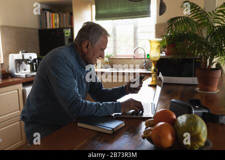 Uomo anziano che usa un computer portatile in cucina Foto Stock