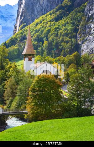 Vista autunnale del Lauterbrunnen Staubbach Falls cascata e il campanile di una chiesa nelle Alpi svizzere, regione di Jungfrau, Svizzera Foto Stock