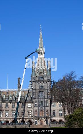 Fettes College Building, Edimburgo, Scozia, Regno Unito. 13th Mar 2020. Addetti alla manutenzione sulla piattaforma di un'enorme gru di controllo che viene effettuata sulla torre dell'orologio dell'edificio storico da lavoratori in cappelli rigidi e giacche gialle. Questa scuola pubblica era notoriamente dove Tony Blair era istruito. Il Collegio è stato fondato nel 1870. Fu progettato da David Bryce, e completato (1864-70) in stile baronale scozzese. Foto Stock