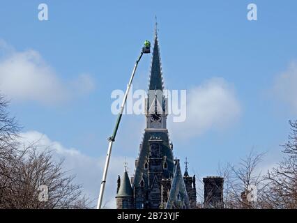 Fettes College Building, Edimburgo, Scozia, Regno Unito. 13th Mar 2020. Addetti alla manutenzione sulla piattaforma di un'enorme gru, verifiche effettuate sulla torre dell'orologio dell'edificio storico da parte di lavoratori in cappelli rigidi e giacche gialle. Questa scuola pubblica era notoriamente dove Tony Blair era istruito. Il Collegio è stato fondato nel 1870. Fu progettato da David Bryce, e completato (1864-70) in stile baronale scozzese. Foto Stock