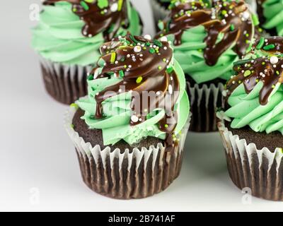 Cupcake al cioccolato con glassa di menta verde e gocce di cioccolato con spruzzette per la giornata di San Patrizio su sfondo bianco! Deliziosa e festosa