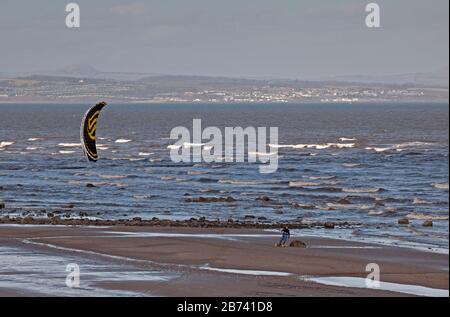 Portobello Beach, Edimburgo, Scozia, Regno Unito. 13th Mar 2020. Uomo Skateboard Kitesurfing lungo la spiaggia di sabbia. Sole ma fresco, Vento: ENE 18 km/h con raffiche di vento di 32 km/h, temperatura di 6 gradi centigradi. Foto Stock