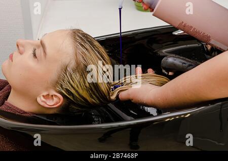 Stylist per capelli applicazione di shampoo colorito viola dopo la tintura dei capelli. Foto Stock