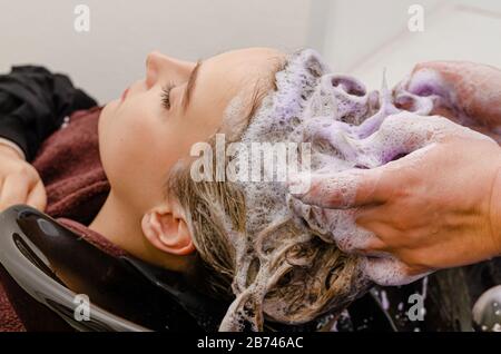 Stylist per capelli applicazione di shampoo colorito viola dopo la tintura dei capelli. Foto Stock