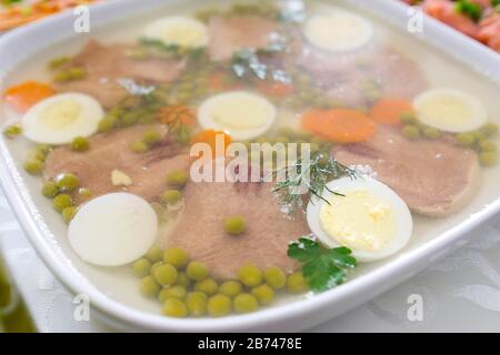 Carne gelata con lingua di manzo, piselli, carote, erbe aromatiche. Un piatto sul tavolo per una festa. Antipasto freddo. Foto Stock