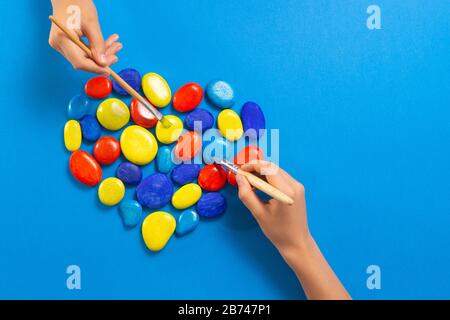 Giornata mondiale di consapevolezza dell'autismo. Bambini mani dipingere con pennelli cuore fatto di pietre nei colori blu rosso giallo Foto Stock