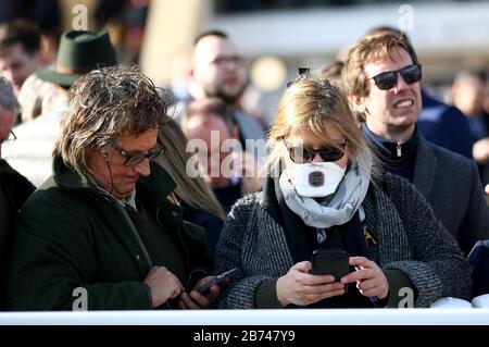 Uno spettatore negli stand che indossa una maschera sulla scia dell'epidemia di coronavirus durante il quarto giorno del Cheltenham Festival all'ippodromo di Cheltenham. Foto Stock