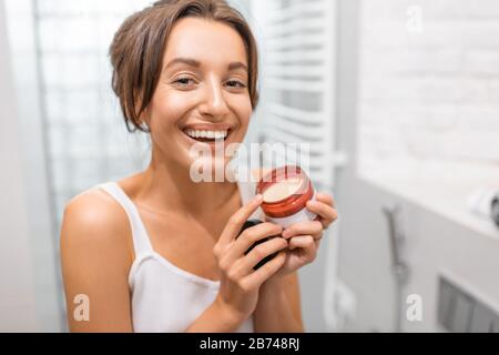 Ritratto di una giovane allegra donna con crema facciale o lozione in bagno. Cura della pelle e concetto di benessere Foto Stock