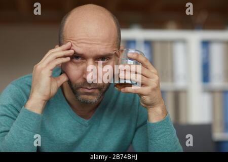 Ritratto di uomo maturo ubriaco che tiene il vetro con il whiskey e che guarda la macchina fotografica con vista triste Foto Stock