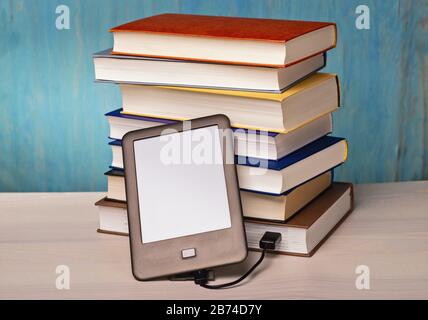 Un lettore di e-book è collegato a una pila di libri tramite cavo USB | utilizzo in tutto il mondo Foto Stock