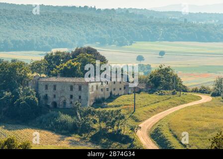 Una vista sulla campagna toscana con una strada tortuosa e una casa dall'esterno di porta Fiorentina, la porta occidentale della fortezza di Monteriggioni, in Toscana Foto Stock