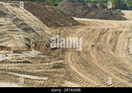 Grande cantiere con pali di terra, sabbia e evidenti tracce di macchinari da costruzione Foto Stock