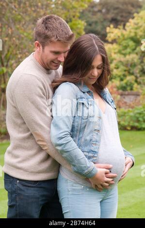 Giovane donna incinta in piedi con la sua partner carezzando il pancino Foto Stock