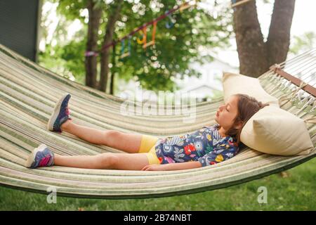 Una bambina si stende su un'amaca da soli al sole con occhi chiusi Foto Stock