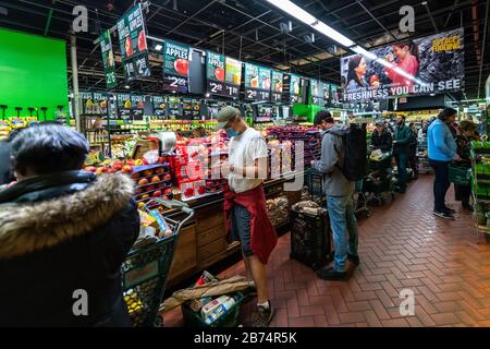 New York, Stati Uniti. 13 Marzo 2020. Gli acquirenti indossano maschere facciali mentre aspettano in fila - fino a un'ora - per pagare i loro generi alimentari in un supermercato di New York City. La folla è andata a fare shopping dopo che la città ha dichiarato emergenza per frenare la diffusione del coronavirus. Credit: Enrique Shore/Alamy Live News Foto Stock