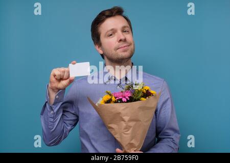 Giovane uomo caucasico in camicia blu che tiene i fiori come regalo per la sua madre o ragazza il compleanno. Anniversario presente concetto. Studio girato su colore Foto Stock