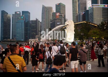 11.08.2018, Singapore, Repubblica di Singapore, Asia - i visitatori cavort a Merlion Park di fronte alla famosa figura di Merlion, la mascotte della città e punto di riferimento. Sullo sfondo sono i grattacieli del quartiere degli affari di Marina Bay con il Centro finanziario di Marina Bay. [traduzione automatica] Foto Stock