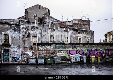 Facciate sbriciolate e contenitori per rifiuti nel centro storico di Catania [traduzione automatica] Foto Stock