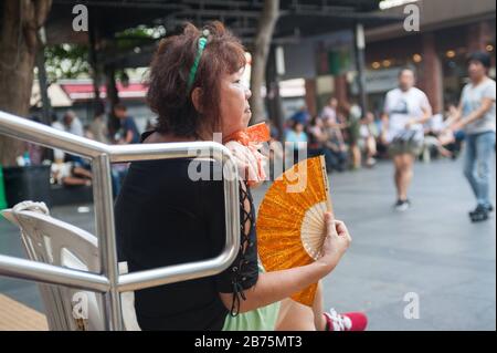 22.10.2017, Singapore, Repubblica di Singapore, Asia - una donna che si fregia con un fan mentre guarda un gruppo di anziani ballare in fila nel quartiere di Chinatown di Singapore. [traduzione automatica] Foto Stock