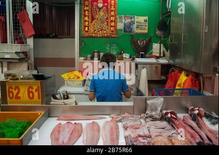 27.07.2017, Singapore, Repubblica di Singapore, Asia - UN venditore di pesce nel mercato di Chinatown sta prendendo una pausa e leggendo il giornale mentre mangia. [traduzione automatica] Foto Stock