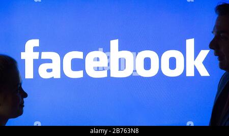 La silhouette di una donna e di un uomo può essere vista di fronte al logo Facebook, su 23.03.2016 [traduzione automatica] Foto Stock